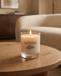 Candle with 'Lucevera' branding on a wooden table in a cozy room.