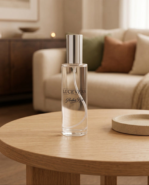 A clear glass perfume bottle with a silver cap stands on a round wooden table in a softly lit living room. The bottle label reads LUCEVERA and appears to be the product being sold.